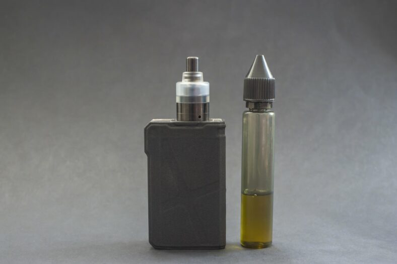 e-zigarette.jpg Ein Verdampfergerät links, daneben eine Flasche mit E-Liquid in einer transparenten Verpackung.