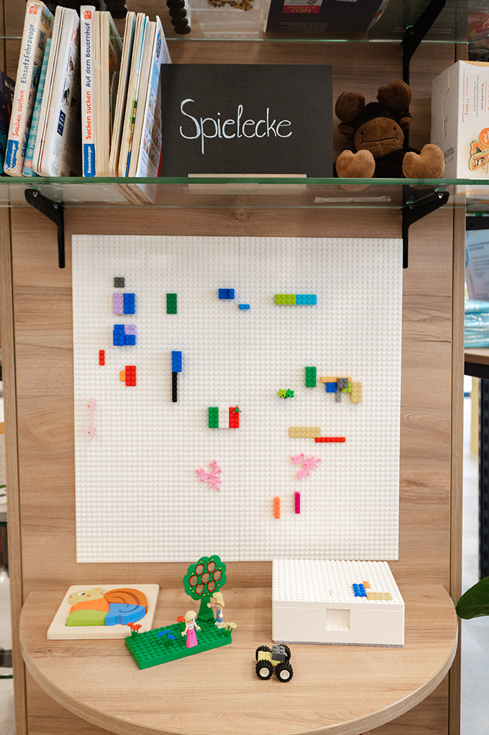Kinderfreundliche Spielecke in der Marien Apotheke Ober-Grafendorf mit Lego-Bauwand, Spielzeugfiguren und Kinderbüchern.