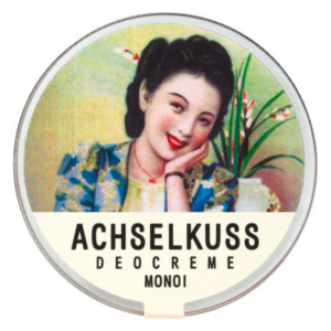 Runde Dose mit einer Frau, die lächelt, und dem Aufdruck "ACHSSELKUSS DEOCREME MONOI".